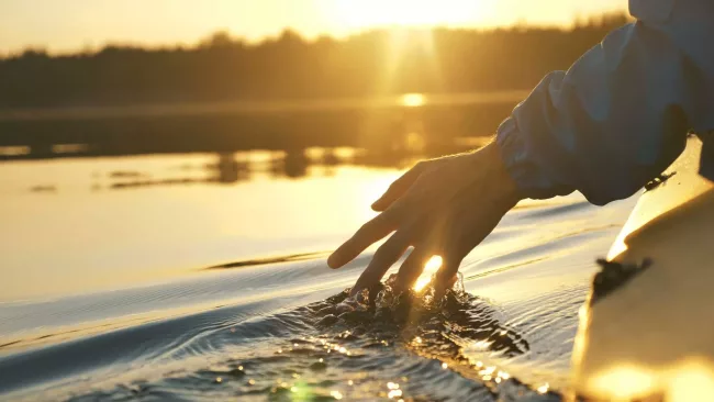 A hand touching water while travelling in a canoe.
